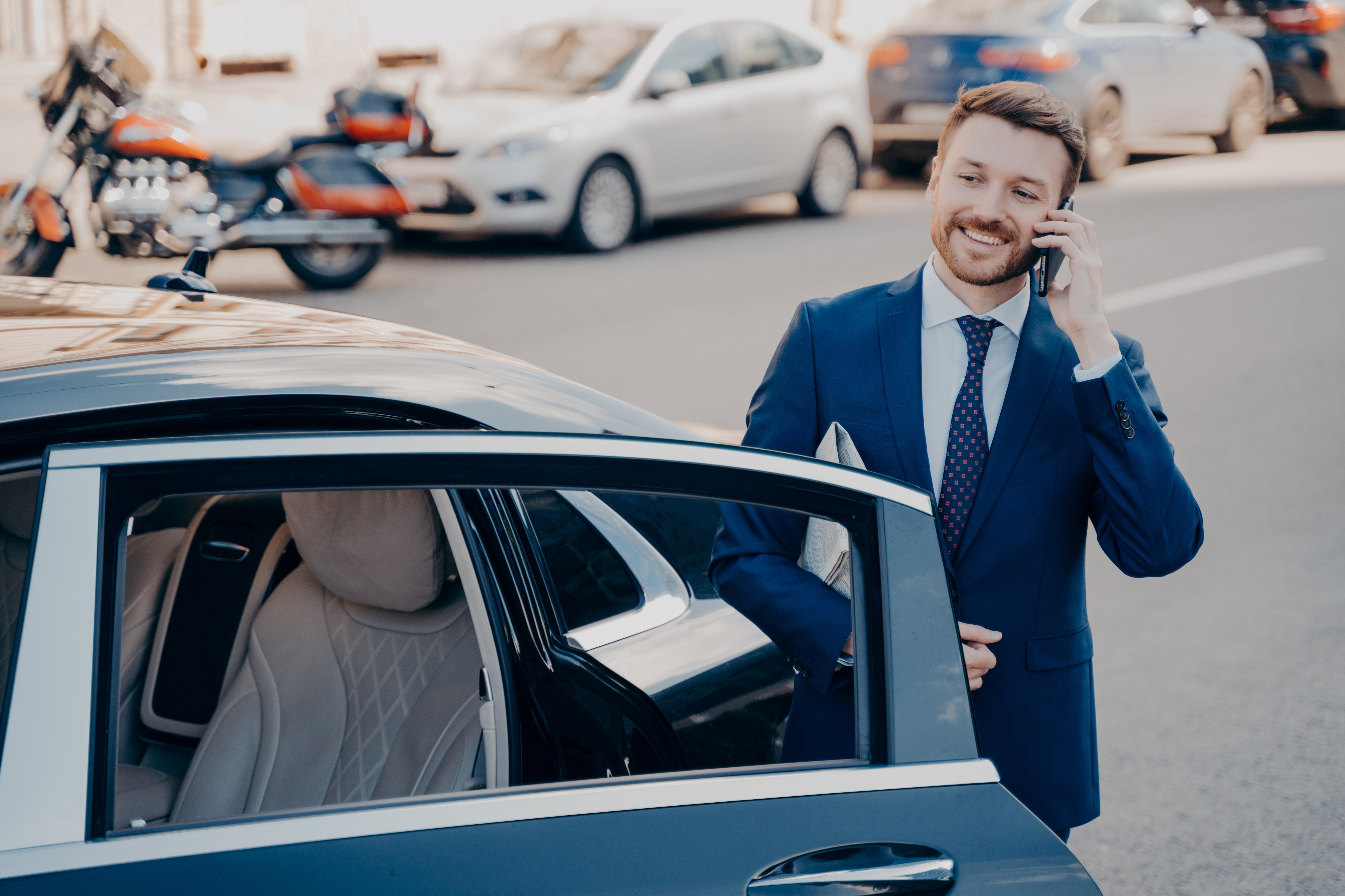 Confident executive talking on phone next to limousine